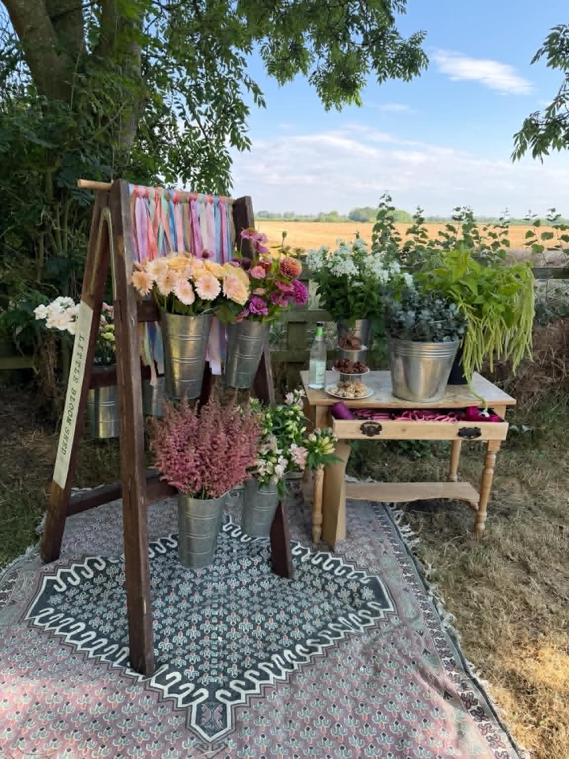 The Little Bloom Bar set up outdoors with a rustic wooden stand and flower buckets