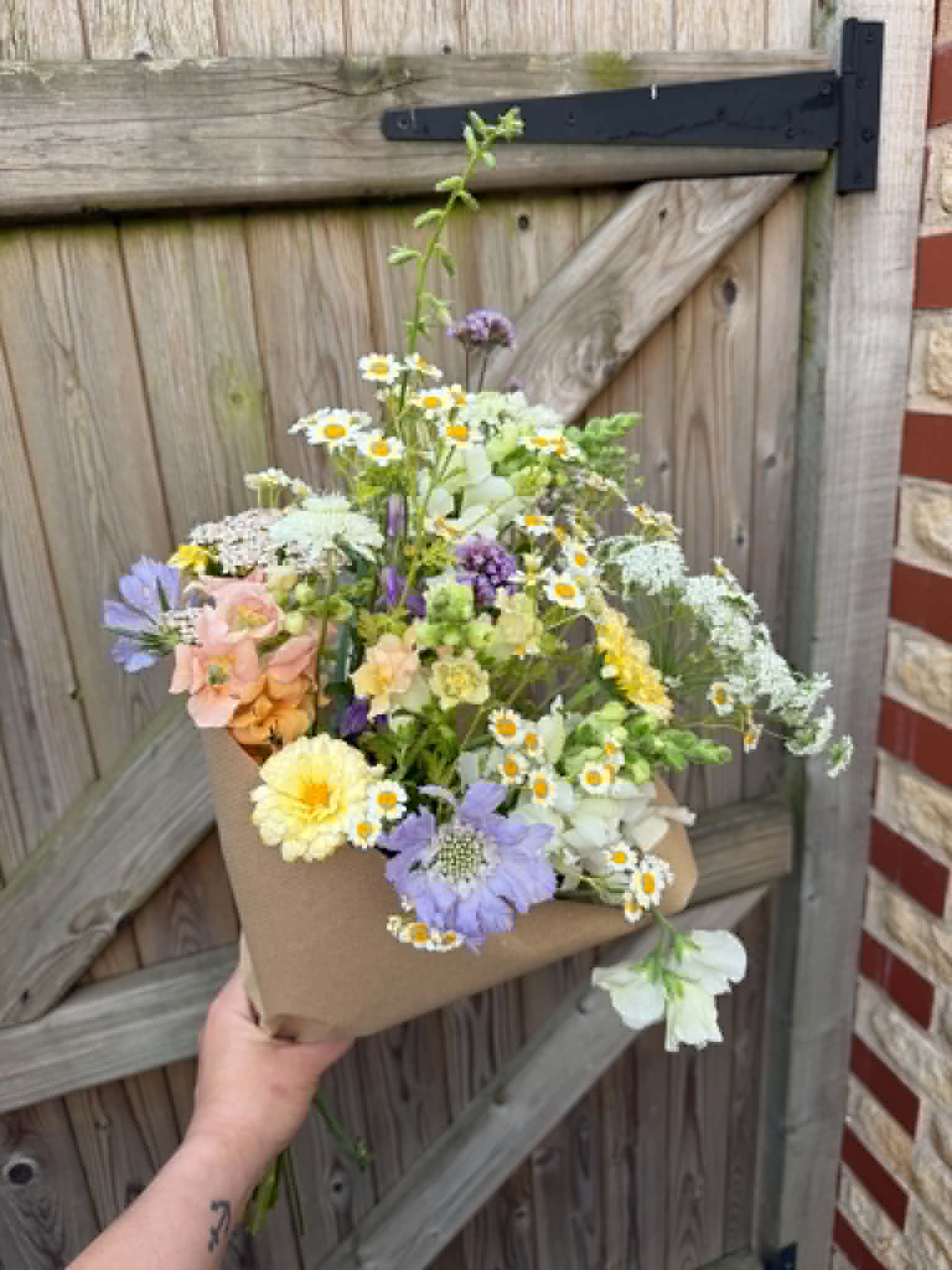 Kraft-wrapped bouquet with chamomile by the garden gate