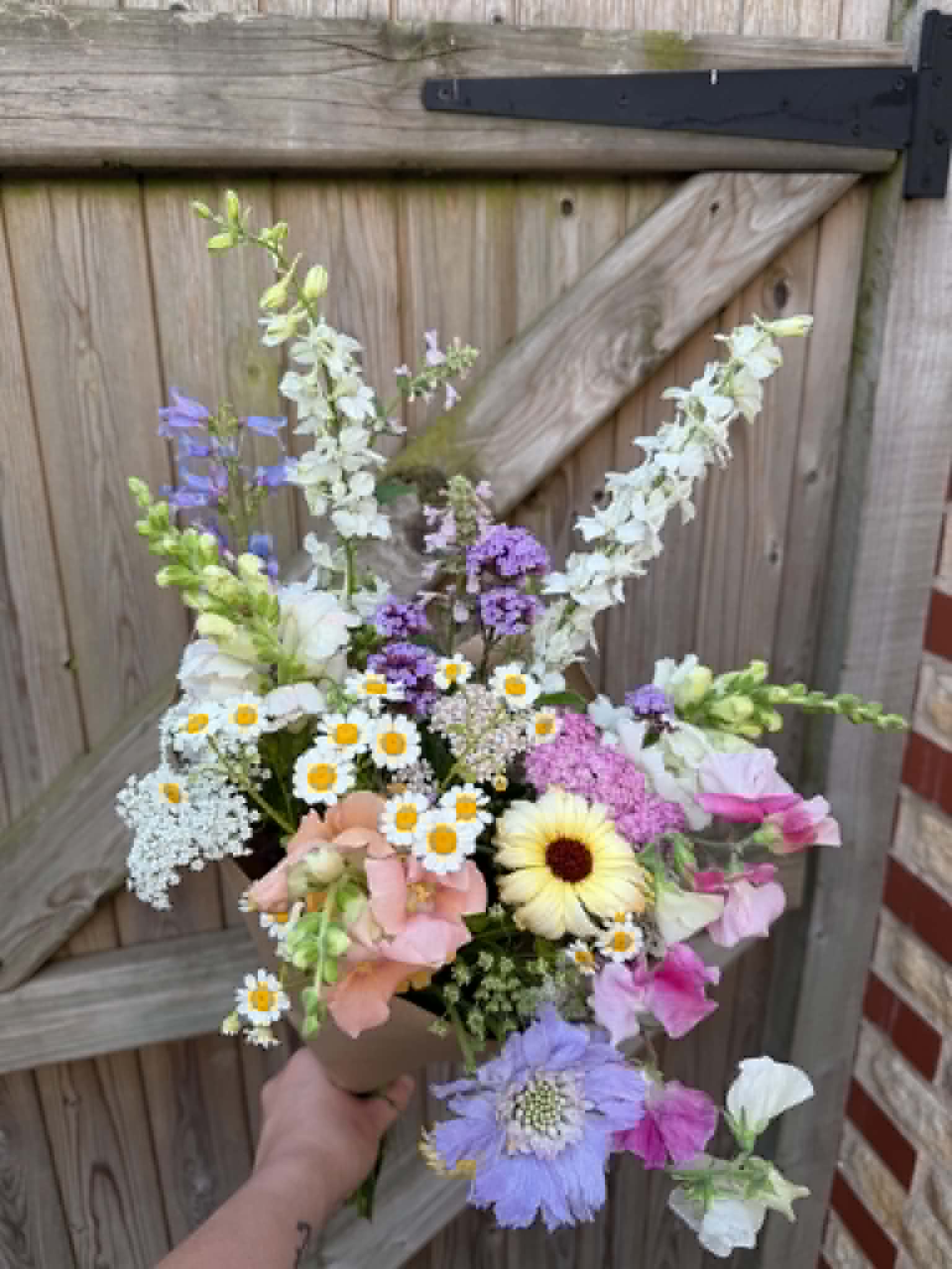 Kraft-wrapped bouquet with delphinium by the garden gate